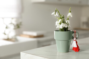 Beautiful snowdrops with traditional martisor on table indoors, space for text. Symbol of first spring day