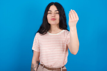 young beautiful tattooed girl wearing pink striped t-shirt standing against blue background Doing Italian gesture with hand and fingers confident expression