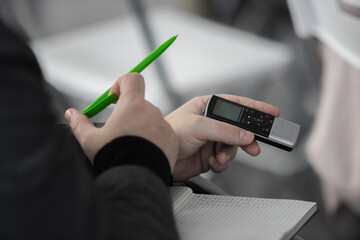 Journalists making news, struggling to get answers. Focus on voice recorder, blurred crowd