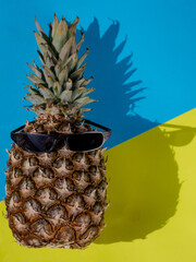 pineapple with sunglasses on a vibrant duotone yellow blue background with hard shadows. vertical, copy space