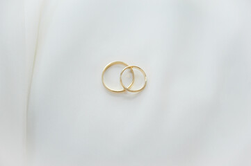 Two gold wedding rings placed together on a white textile surface with copy space.