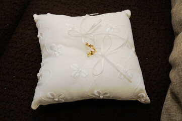 Two gold rings together on a small white cloth cushion.