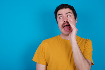 young handsome Caucasian man with moustache wearing orange t-shirt against blue background hear incredible private news impressed scream share