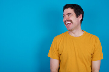 young handsome Caucasian man with moustache wearing orange t-shirt against blue background very happy and excited about new plans.