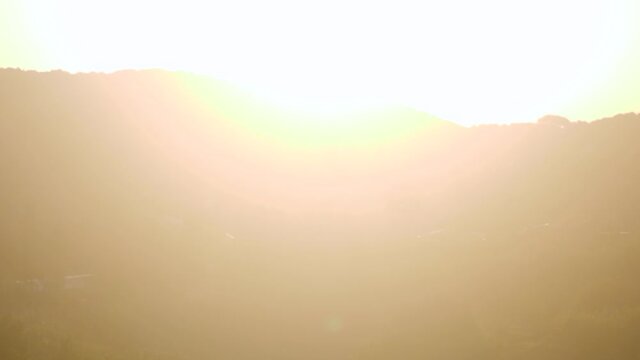 Young caucasian man looking at hills with the sun making lens flares in camera - pan right