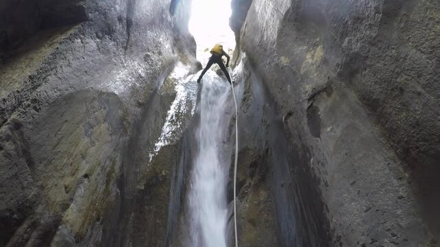 Low angle view: Man with yellow pack rappelling river canyon waterfall