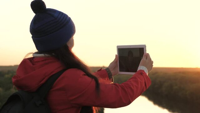 Young woman tourist blogger records selfie video of peak of mountain using tablet computer against background of beautiful landscape of. Carefree cheerful girl travels and takes pictures of nature