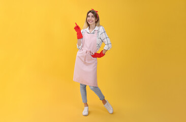 Young housewife in gloves on yellow background