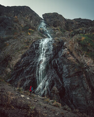 Russia, Caucasus, Dombay, Sofrujuk (Sofrujinsky) waterfall, high in the evening light, dramatic landscape, tourist on the background of the waterfall