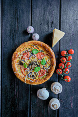 Hot homemade pizza with tomatoes, mushrooms, mozzarella, sweet pepper and Basil on a black background. Snack. Pizzeria. Vertically. Copy space.