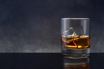 A glass of whiskey or cognac with two ice cubes. Smoke in the background.