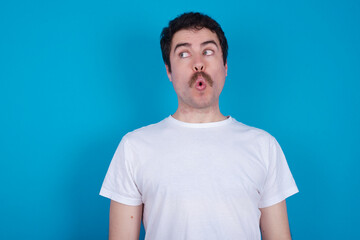Fototapeta premium Shocked young handsome Caucasian man with moustache wearing white t-shirt against white background look empty space with open mouth screaming: Oh My God! I can't believe this.