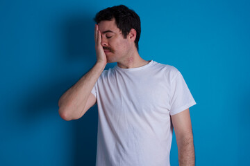 Afraid funny young handsome Caucasian man with moustache wearing white t-shirt against white background holding telephone and bitting nails