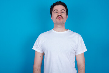 Obraz premium Portrait of lovely funny young handsome Caucasian man with moustache wearing white t-shirt against white background sending air kiss