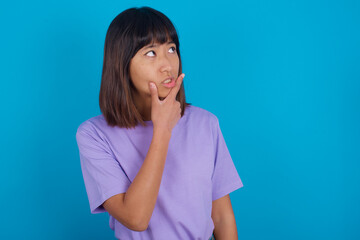 Young beautiful asian girl wearing purple t-shirt against blue background Thinking worried about a question, concerned and nervous with hand on chin.
