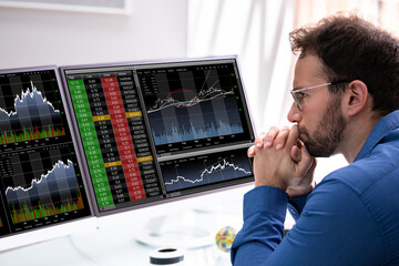 Stock Market Broker Looking At Graphs On Multiple Screens