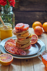 Pancakes with red oranges on a wooden background. Side view.