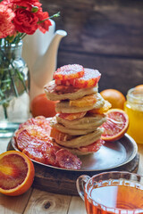Pancakes with red oranges on a wooden background. Side view.