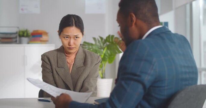 Angry african male boss shouting at young female employee pointing at report mistake