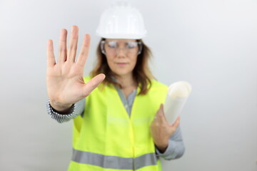 Woman engineer with hardhat holding plans under arm and with open hand doing stop sign with serious and confident expression, defense gesture. Face bokeh.