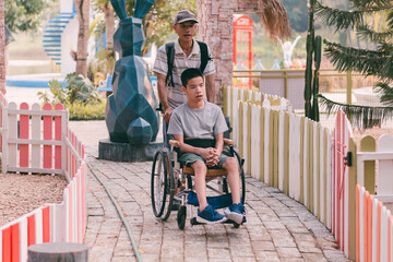 Disabled child sitting on wheel​chair​ and father have fun with activity on the outdoor park on...