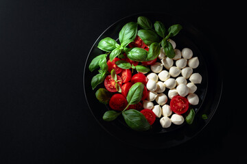 Caprese salad with tomato, mini mozzarella and basil on a black plate.