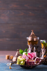 Bowl with various pieces of turkish delight lokum and black tea with mint on a dark background.