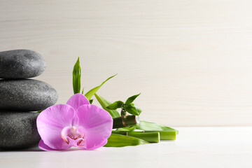 Spa stones, bamboo stems and beautiful orchid flower on white table, space for text