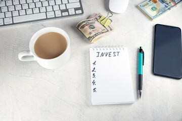 INVEST written in notebook, wad of dollars money cash in elastic band copy space background,concept of wealth builder mindset,remind self to set small amount of money to invest and grow to save