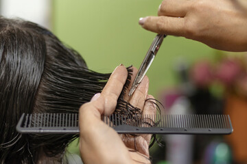 female hands doing a haircut on dark hair.