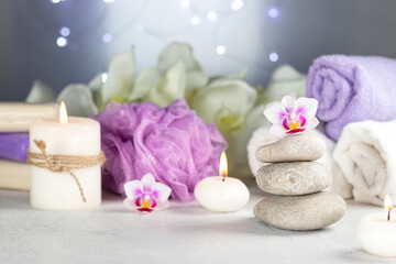 Fototapeta na wymiar massage stones, burning candles, rolled towels, flowers, abstract lights. Spa resort therapy composition in lilac colors