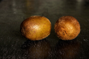 Fototapeta premium Two ripe whole kiwi fruits on a black wooden surface.