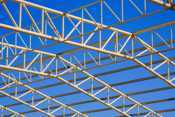 Low angle view of yellow metal building roof structure in construction area against blue sky background