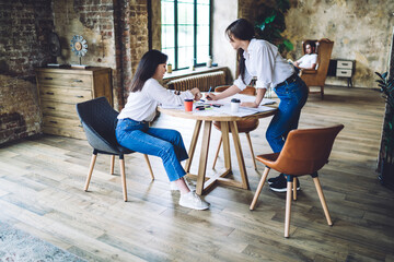 Focused young women drawing placard on table in creative workspace