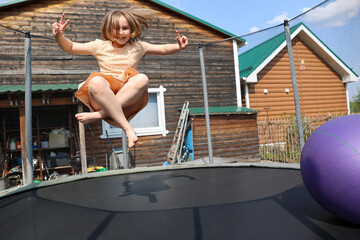 Joyful little girl with a smile on her face in a beautiful dress jumping on the trampoline