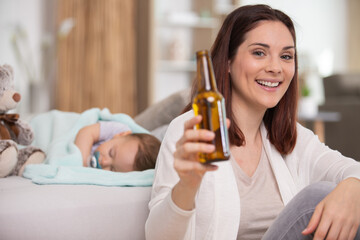 carefree woman drinking beer while baby is sleeping