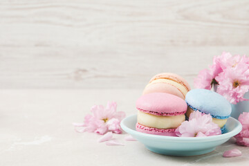 Obraz na płótnie Canvas Delicious colorful macarons and pink flowers on light grey table, space for text