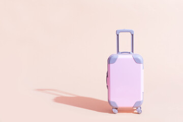 Obraz premium Pink Suitcase toy on a peach, sandy background. Minimalism and travel concept