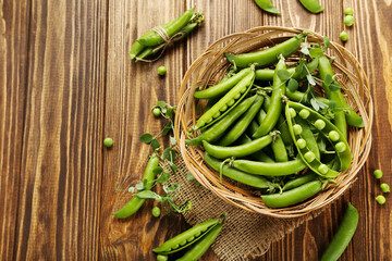 Green pea pods in basket on brown wooden table