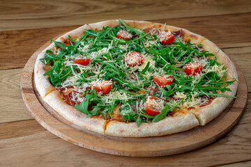 Pizza with prosciutto parma ham, arugula salad rocket, cherry tomatoes and parmesan on wooden background. Italian cuisine. Neopolitan pizza