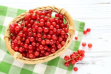 Red currants in basket with napkin on white wooden background