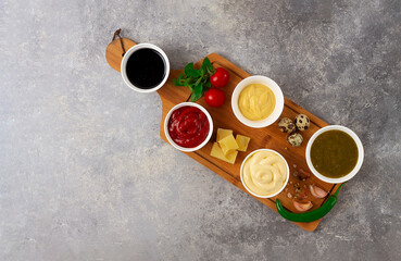Obraz na płótnie Canvas Set, assortment of sauces, ketchup, mayonnaise, cheese, soy, green, on a cutting board, with ingredients, on a gray table, top view, no people,
