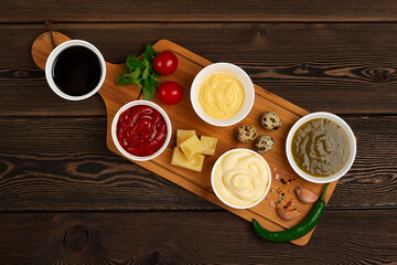 Assortment of sauces, ketchup, mayonnaise, cheese, soy, green, on a cutting  board, with ingredients, on a wooden background, top view, no people,