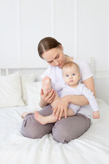 an anxious mother with a baby in her arms holds the baby's leg on the bed at home