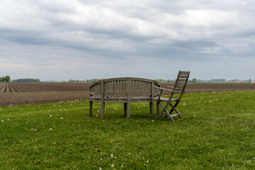 wooden garden furniture on a green field under an overcast sky with a freshly plowed field behind