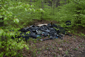 Illegal garbage dump inside forest. Garbage in forest. Car parts dump. Parts from a stolen car. Plastic pollution in forest.