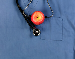 Good health concept with stethoscope and apple placed on blue medical outfit in close up view