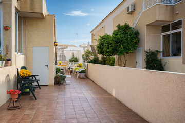 Backyard paved patio with plastic chairs, table, umbrella, flowers, ceramic pots, tangerine trees...