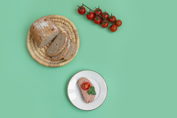 Breakfast sandwich with pate, tomato and greens served on white plate. Green background, top view, copy space.