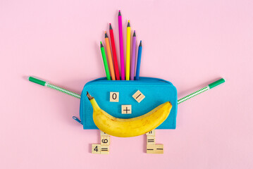 Bright multicolored school supplies, stationery and a banana in the form of a smiling character on a pink background. Back to school, preschool education. Fun mathematics. School lunch or breakfast. 